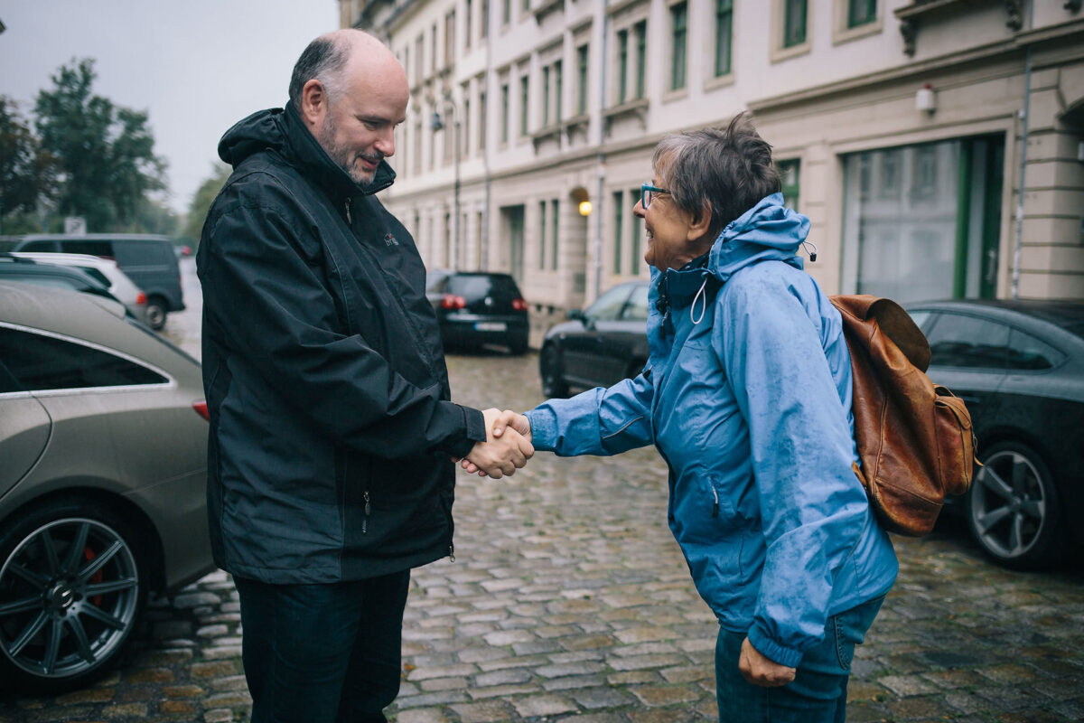 deutschland spricht older man and older woman shaking hands outside